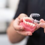 Orthodontist holding lower human jaw model and transparent aligners in modern educational clinic